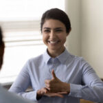 Smiling young Indian woman who is deaf using sign language, communicating with friend or doctor physician, happy attractive female having fun and enjoying pleasant conversation, hard of hearing